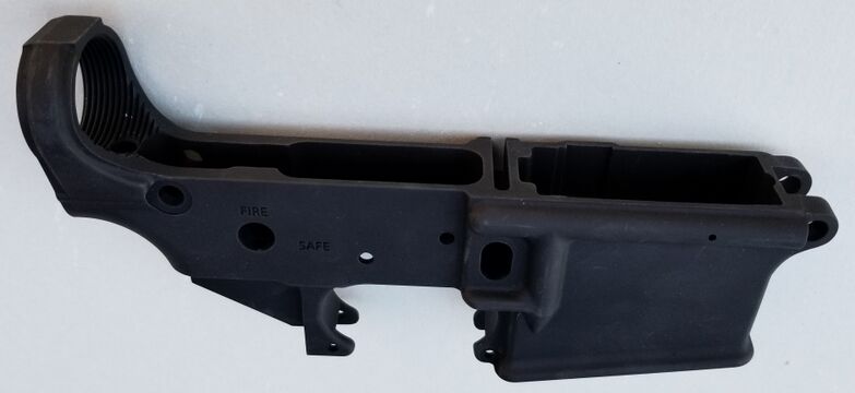 A stripped AR-15 lower receiver: the magazine well, fire-control pocket, threaded buffer-tube boss, and pin holes. Wikimedia Commons (Thewellman, CC0).
