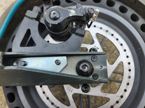 Under the outer cover: the metal axle bracket with the central wheel axle hardware (capped) flanked by two more recessed security Torx screws, top and bottom. The owner described these underneath screws as a different size from the cover screws, needing a second bit before the axle would come apart.