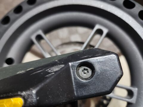 The first fastener the owner hit: a security Torx screw holding the cover over the rear axle, recessed in the black plastic dropout cover with the worn tire behind it. The raised pin in the center of the star blocks an ordinary Torx or hex bit from seating, so her tools would not bite.