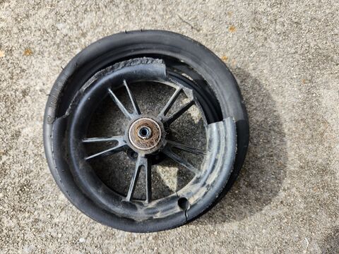 The rear wheel after removal, on the driveway. The inner tube is gone after the tire has worn through along the tread and split open, the failure that started the repair. Per the owner the scooter was bought new and this tire gave out in under eighteen months. Changing a tire does not touch the battery pack or any safety-rated part.
